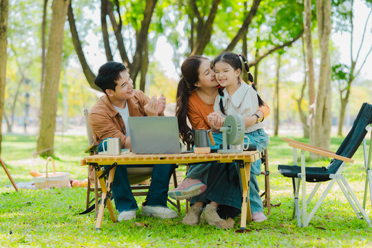 A family of three from Asia enjoyed using their laptops in the park and also enjoyed a picnic together in the park.