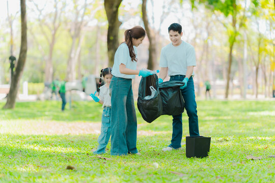 Environmental conservation concept: A cute little girl and her parents are picking up trash in the park. A family of volunteers is collecting trash in the forest. Environmental conservation concept.