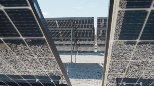 Photovoltaic bifacial panels mounted over reflective white stone ground. Solar modules using albedo effect for power generation efficiency. Renewable energy infrastructure and engineering.