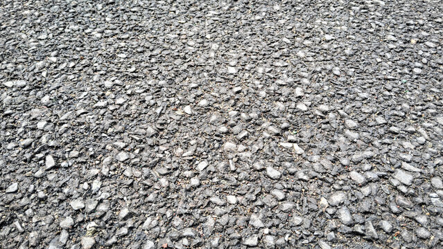 High-angle close-up of rough dark gray asphalt road surface texture, grainy bitumen pavement background with crushed stones and gravel details.