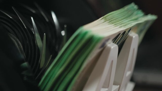 Close-up view of a cash counting machine processing banknotes, showcasing the continuous flow of currency through the device in a well-lit indoor setting