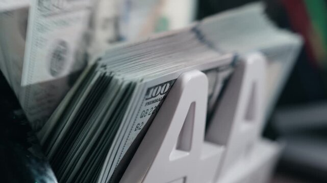 Stack of U.S. dollar bills organized in a money holder, showcasing the sequential arrangement of cash in a financial office setting with blurred background elements