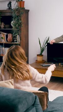 Happy family having fun together playing charades in their living room. An elderly man is gesturing while the women are guessing and cheering. Vertical