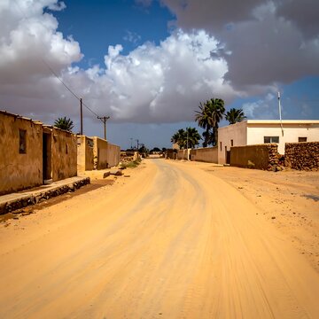 A deserted dirt road with buildings on either side under a cloudy sky