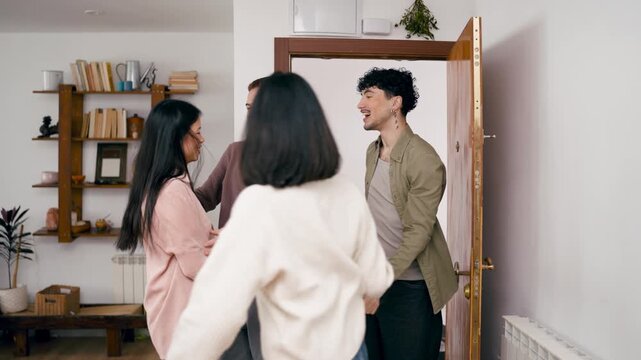 Smiling young couples welcoming friends at the front door. Happy friends meeting and hugging each other with joy in a cozy apartment