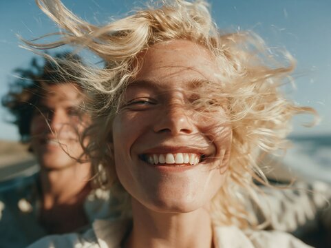 Joyful couple with windblown hair enjoying a sunny day at the beach