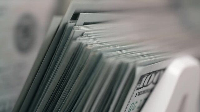 Close-up sequence of stacked hundred-dollar bills in a cash drawer, showcasing the detailed texture and arrangement of the currency in a financial setting