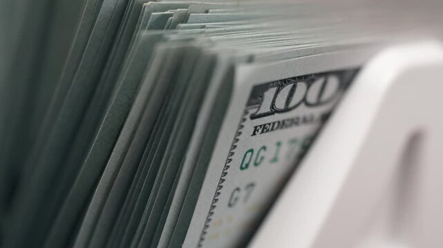 Stack of US 100 dollar bills being counted inside electronic money counter machine. Concept financial accuracy and cash management systems.
