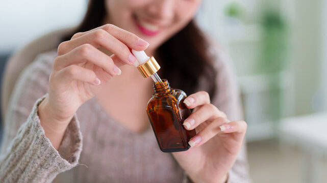Asian women holding amber glass dropper bottle applying facial serum skincare treatment beauty routine at home wellness self care organic cosmetic product