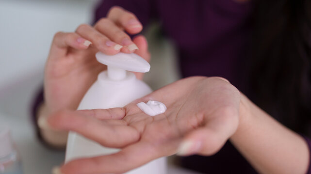 woman hands dispensing white moisturizer cream lotion from pump bottle applying skincare beauty product for daily face body hydration wellness routine at home