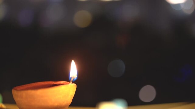 Macro shot of flame from cotton oil soaked wick in a earthenware clay diya set against a background with light bokeh showing the simple traditional decorations during diwali in India