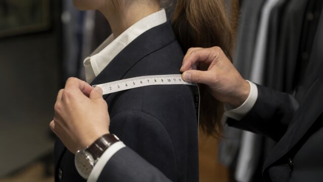 A tailor measures a woman"s shoulder for a fitted suit, showcasing attention to detail in the tailoring process.