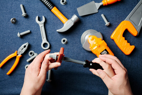 Close-up of father and child hands working together with a toy screwdriver and bolt. Concept of fatherhood, teaching, and passing down skills through play