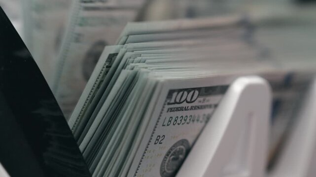 Money counter machine counting stack of 100 dollar bills in close-up, focus on fast movement of cash. Concept cash flow and financial technology.
