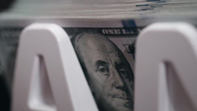 Close-up sequence of US dollar bills stacked in a white money holder, showcasing the detailed portrait of Benjamin Franklin and the texture of the currency