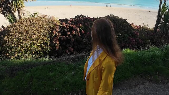 A woman walks on the evening seaside wearing yellow jacket