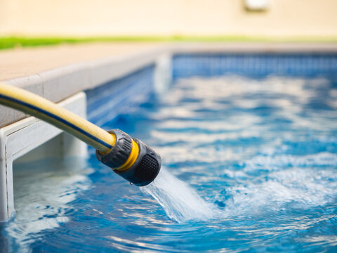 Garden hose filling swimming pool with clear blue water - summer maintenance concept