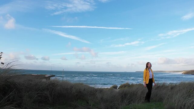 A woman walks on the evening seaside wearing yellow jacket