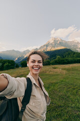 Naklejka premium Cheerful woman outdoors, smiling into the camera, backpack ready for a hike, wide green meadow with distant mountains, soft light, natural colors, relaxed lifestyle moment today