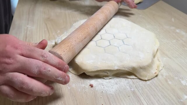 Closeup of hands rolling pastry dough on floured wooden table, honeycomb cutter pattern pressed in dough, cozy homemade baking mood, food prep detail