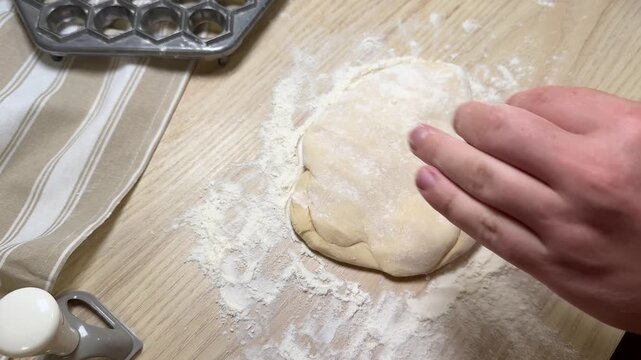 Hand shaping dough on floured wooden table, baking tools nearby in home kitchen, warm practical mood for cooking and meal preparation
