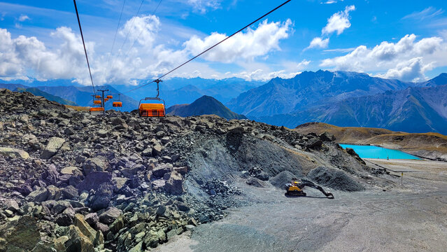 Ischgl, Austria - August 18, 2022. View from Tirol Alps with cable car with orange cabins, crawler excavator Volvo and picturesque alpine emerald lake.