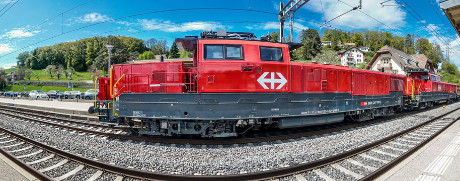 SBB Cargo red locomotive on railway tracks at Puidoux station with Swiss countryside in background in Switzerland.
