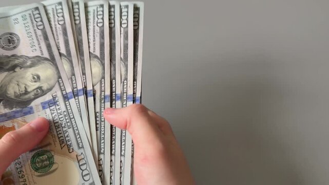 Hands holding and fanning out a large stack of one hundred US dollar bills. Concept of financial abundance, high income, wealth exhibition, and successful business investment.