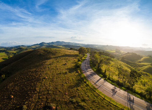 Estrada de montanha cortando paisagem verde em Minas Gerais ao entardecer.