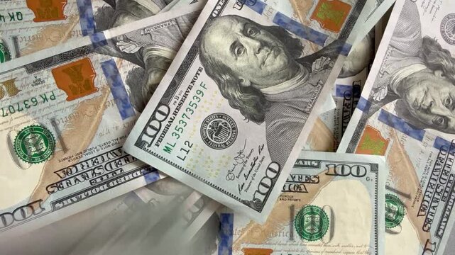 Close-up of one hundred dollar bills falling onto a pile of US currency. Concept of wealth, rain of money, financial success, economic growth, and big profit.