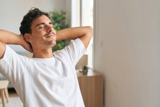 Young man relaxing at home, smiling with hands behind head