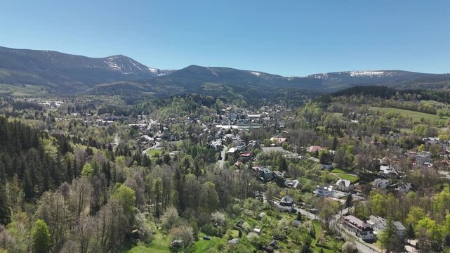 Aerial view of a mountain town in a valley with snow capped peaks of Karkonosze Mountains Poland in spring