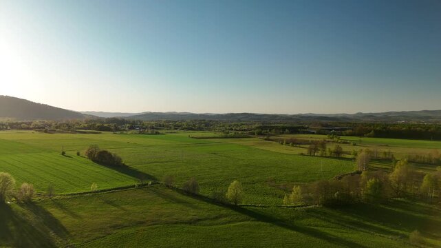 Aerial view of green meadows and fields with forested hills on the horizon at sunset in spring