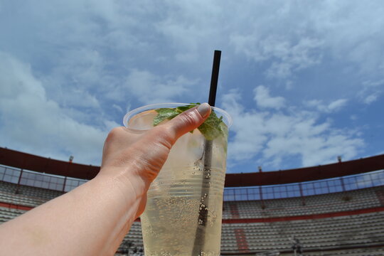 Hand holding rebujito cup against blue sky and bullring at feria de abril for festival poster and beverage promotion