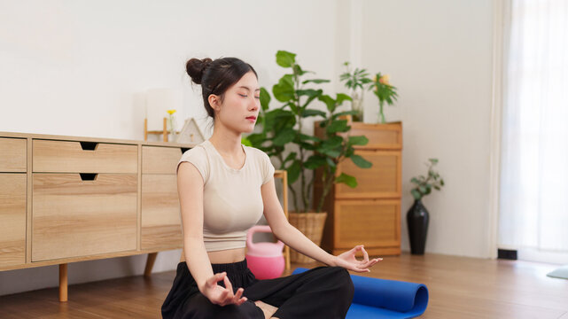 young Asian women meditation yoga exercise fitness wellness at home sitting lotus position wooden floor living room mindfulness relaxation healthy lifestyle