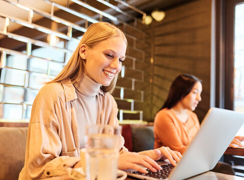 Woman smiling, holding coffee while working on a laptop having an online meeting conferance call  in a cafe