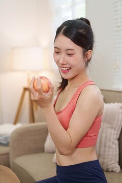 young Asian women holding fresh apple smiling healthy eating lifestyle wellness nutrition fitness sportswear living room home bright morning light casual