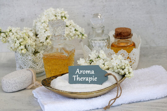 Aromatherapie-Stillleben mit &auml;therischen &Ouml;len, Fliederbl&uuml;ten, Badesalz und wei&szlig;em Handtuch.
