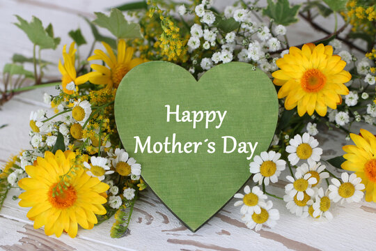 Mother's Day greeting with a green wooden heart and yellow spring flowers on rustic wood.