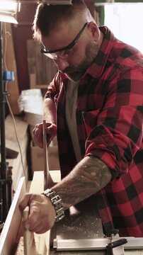 Vertical video. Woodworking process. Jointer machine. Male carpenter guiding plank with push pad on professional power electric equipment.