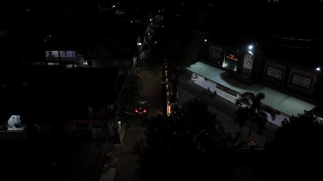 Aerial view panning across a dimly lit street and a mosque building during nighttime in Indonesia.