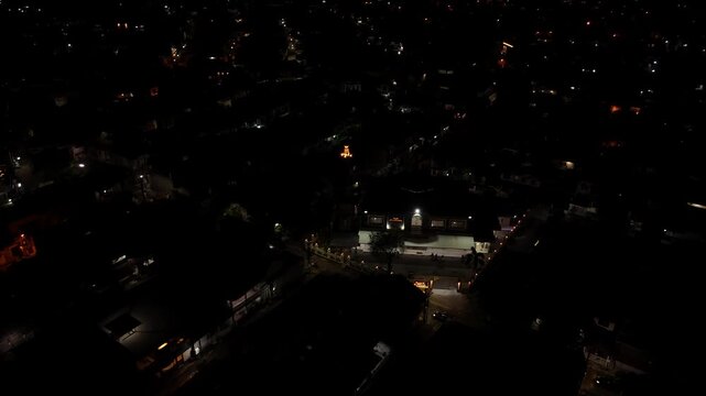 Drone shot pulling back from a lit mosque and community gathering at night in a residential area.