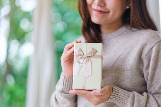 Closeup image of a woman in sweater holding a present box at home