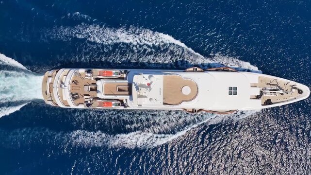 Aerial drone tracking video of beautiful modern super yacht with wooden deck cruising in low speed deep blue Mediterranean sea