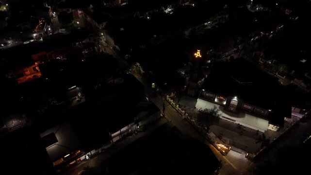 Cinematic aerial rotation around a lit mosque minaret at night overlooking a dark city landscape.