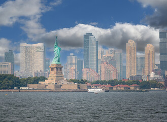 Obraz premium New york, usa august 16,2024. Iconic statue of liberty rising over liberty island with manhattan skyline and harbor under a bright blue summer sky, wide view