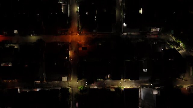 Overhead drone shot moving slowly over dark city rooftops and illuminated streets at night in Indonesia.