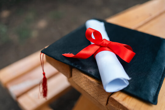 Graduation cap with diploma and red ribbon on wooden bench education achievement concept