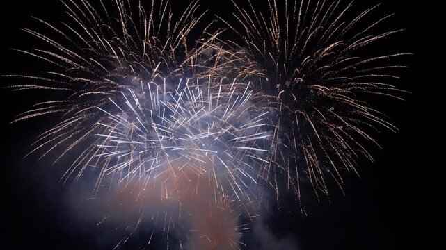 Spectacular fireworks display illuminates dark night sky with brilliant golden and white bursts exploding simultaneously.