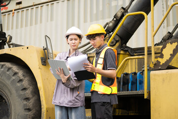 Fototapeta premium Two operation or engineer construction supervisor is checking on heavy machine and equipment checklist form with crane truck as background. Industrial safety working in action